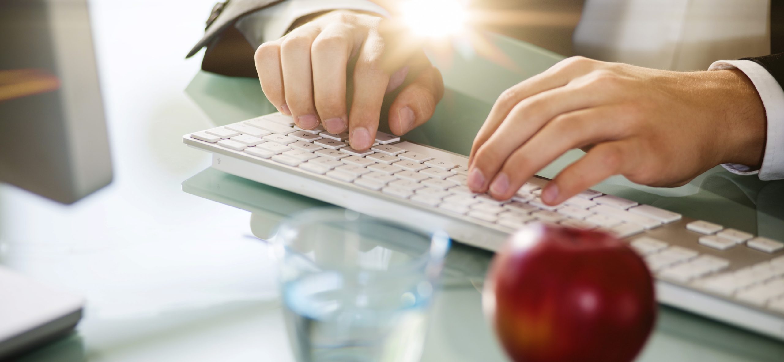 Geschftsmann mit Flares  tippt auf Tastatur mit Apfel und Glas Wasser